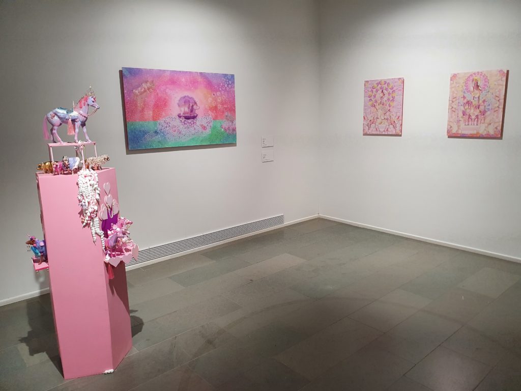 Kuvassa installointinäkymä Tampereen taidemuseon näyttelysalista, jossa vasemmalla näkyy vaaleanpunainen viisikulmainen jalusta, jolle Idolien hahmoja on installoitu. Idoleista vasemmalle näkyvät teokset Venus ja Marshmallow monuments.